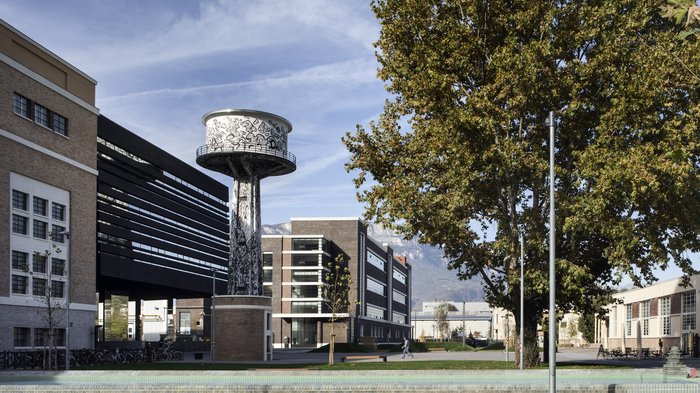 Avviata la procedura a evidenza pubblica per l’insediamento di imprese attraverso l’edificazione privata al NOI Techpark di Bol-zano Vista urbana con torre d'acqua decorata e edifici moderni sotto un cielo limpido