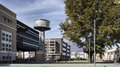 Avviata la procedura a evidenza pubblica per l’insediamento di imprese attraverso l’edificazione privata al NOI Techpark di Bol-zano Vista urbana con torre d'acqua decorata e edifici moderni sotto un cielo limpido
