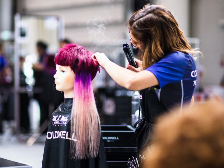 Friseure Friseurin stylt pink-violette Haare einer Übungspuppe mit einem Glätteisen