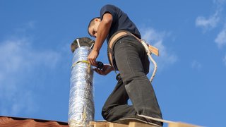 News Handwerker installiert isoliertes Rohr auf Dach bei klarem Himmel