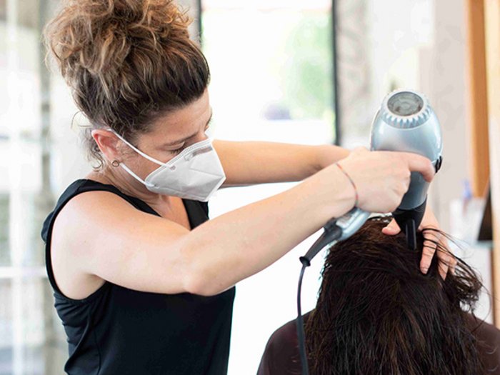 Friseure besser und stärker geschützt Friseurin mit Maske föhnt Haare einer Kundin im Salon