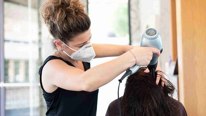 Friseure besser und stärker geschützt Friseurin mit Maske föhnt Haare einer Kundin im Salon