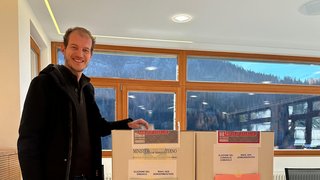 News Mann wirft seinen Stimmzettel in eine Wahlurne in einem hellen Raum mit Bergblick