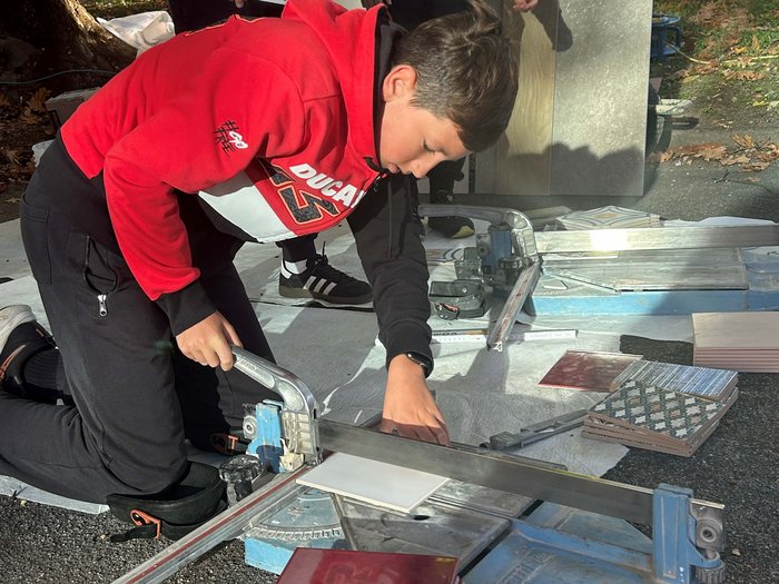 SkillsDay in Lana: Schüler/innen erleben Handwerk hautnah Junge schneidet Fliesen mit Fliesenschneider im Freien