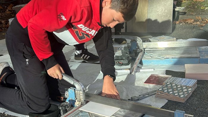 SkillsDay in Lana: Schüler/innen erleben Handwerk hautnah Junge schneidet Fliesen mit Fliesenschneider im Freien