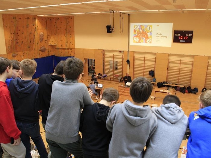 Schulprojekt "Clever gebaut": Preisverleihung am 29. April in Meran Junge beobachten Preisverteilung in Turnhalle mit Anzeigetafel und Präsentation