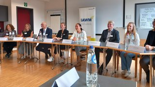 News Menschen sitzen an einem Tisch bei einer Besprechung vor IAWM-Banner