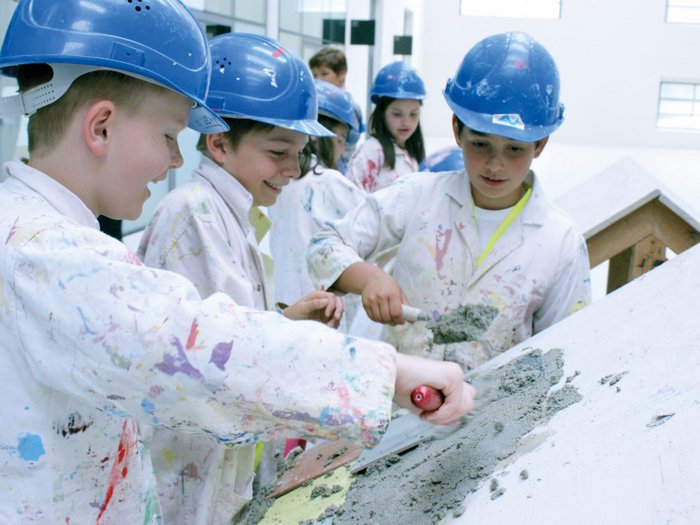 Erlebniswelt Baustelle Kinder in Schutzhelmen bearbeiten Beton auf einer geneigten Oberfläche