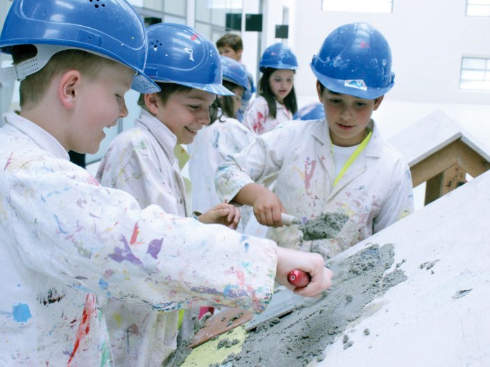 Erlebniswelt Baustelle Kinder in Schutzhelmen bearbeiten Beton auf einer geneigten Oberfläche