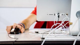 News Hand am Computermaus neben einem Monitor auf einem Schreibtisch