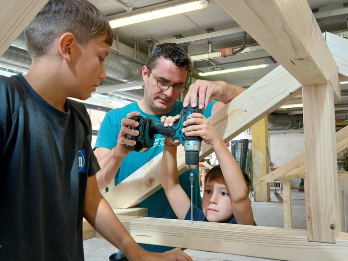 Handwerk zum Anfassen: KidsAcademy begeistert Kinder in Schlanders Mann hilft Jungen beim Bohren in Holzrahmen in einer Werkstatt