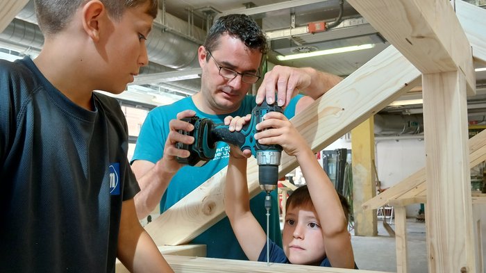 Handwerk zum Anfassen: KidsAcademy begeistert Kinder in Schlanders Mann hilft Jungen beim Bohren in Holzrahmen in einer Werkstatt