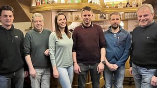 News Sechs Personen stehen in einer Bar vor einem Holzregal mit Gläsern und Flaschen