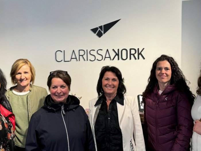Grenzüberschreitend Netzwerken Sechs lächelnde Frauen stehen vor einer Wand mit dem Clarissa Kork Logo