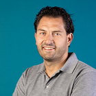 Heizungs-, Lüftungs- und Sanitärtechniker Porträtfoto eines lächelnden Mannes in grauem Poloshirt vor blauem Hintergrund