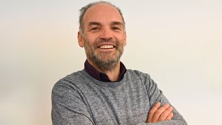 News Lächelnder Mann mit grauem Pullover vor weißem Hintergrund