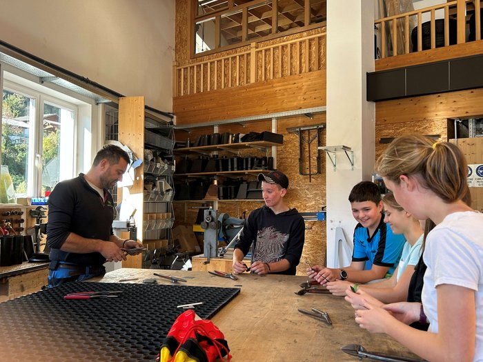 Entdeckungsreise in Berufe des Handwerks und Gastgewerbes an der Mittelschule St. Martin in Passeier Lehrer erklärt Werkzeugtechnik einer Gruppe Jugendlicher in Werkstatt
