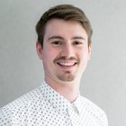 Kommunikationstechniker Porträt eines lächelnden jungen Mannes mit gemustertem Hemd vor grauem Hintergrund