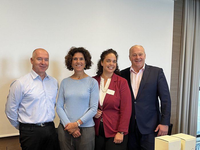 Incontro tra i meccatronici d'auto di quattro Paesi Quattro persone in piedi affiancate davanti a una parete bianca sorridono alla fotocamera