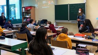 News Schüler und Lehrerin im Klassenzimmer mit Masken während des Unterrichts