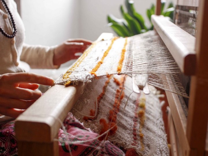 Magliai, ricamatori e tessitori Persona tessendo su un telaio con fili colorati in una stanza luminosa