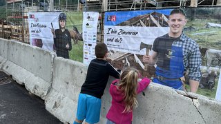 News Zwei Kinder schauen sich Bauplakate mit Handwerksberufen auf einer Baustelle an