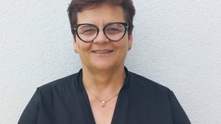 News Porträt einer lächelnden Frau mit kurzen Haaren und Brille vor weißer Wand