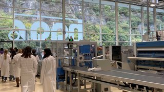 News Menschen in weißen Kitteln in einer Fabrikhalle mit Maschinen und Kartons