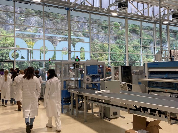 Attraverso la Bassa Atesina alla scoperta dell’artigianato Persone con camici bianchi in una fabbrica con macchinari e scatole