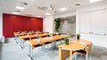 Vermietung Seminarräume Heller Schulungsraum mit Holztischen, roten Stühlen und Wasserflaschen