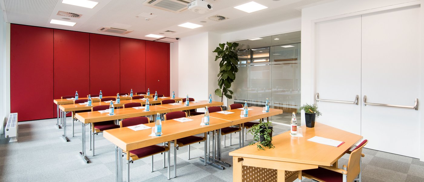 Affitto aule seminari Aula luminosa con tavoli in legno, sedie rosse e bottiglie d'acqua