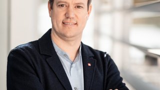 News Porträt eines lächelnden Mannes mit verschränkten Armen im modernen Büro