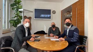 News Drei Männer mit Masken bei einem Meeting am Tisch in einem Büro