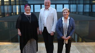 News Drei lächelnde Personen in einem modernen Gebäude mit Glasdach