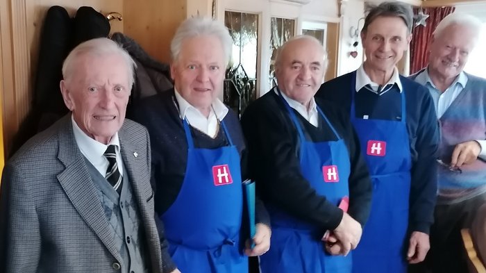 Die Althandwerker/innen des lvh feiern ihren Altehrenpräsidenten Sebastian Brugger. Er ist 95 geworden. Fünf ältere Männer, drei in blauen Schürzen mit H-Logo, in einem Raum