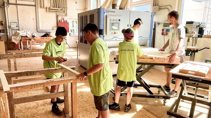 © lvh.apa Jugendliche und ein Erwachsener arbeiten an einer Holzwerkstatt mit Maschinen