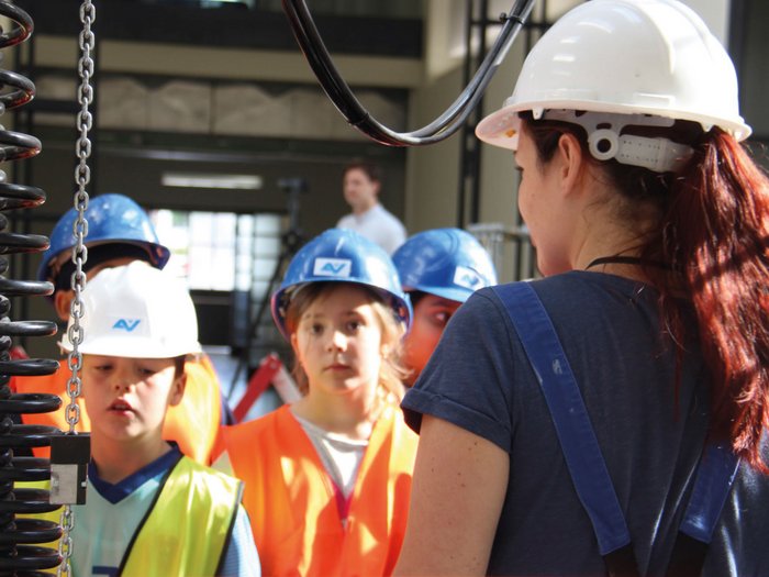 Erlebniswelt Baustelle Frau erklärt Kindern in Schutzhelmen und Warnwesten Sicherheitsregeln in Industrieumgebung