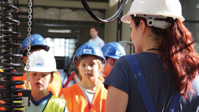 Erlebniswelt Baustelle Frau erklärt Kindern in Schutzhelmen und Warnwesten Sicherheitsregeln in Industrieumgebung