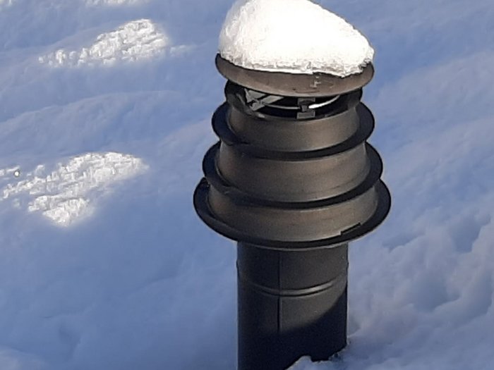 Schnee auch für Kamine problematisch Schwarzes Lüftungsrohr mit Schneekappe im Schnee