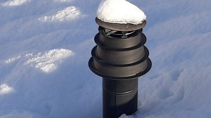 Schnee auch für Kamine problematisch Schwarzes Lüftungsrohr mit Schneekappe im Schnee