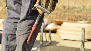 News Person hält Hammer mit Arbeitshandschuhen auf einer Baustelle