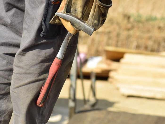 Öffentliche Ausschreibungen: weitere Erleichterungen für Unternehmen angepeilt Person hält Hammer mit Arbeitshandschuhen auf einer Baustelle