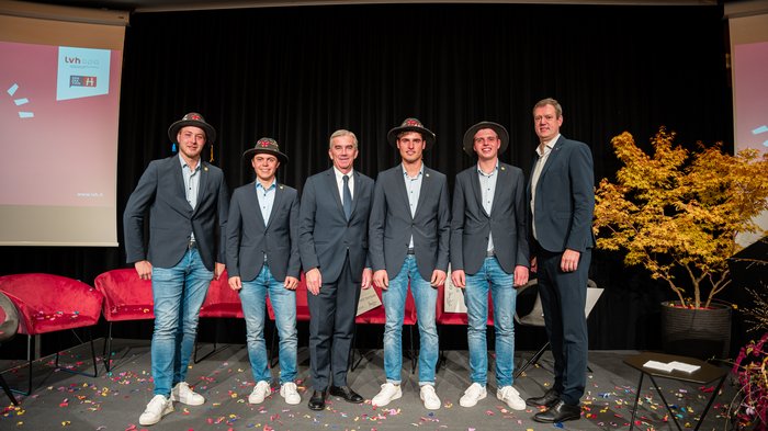 Giornata dell'artigianato Sei uomini in abito, quattro con cappelli tradizionali, su palco con coriandoli