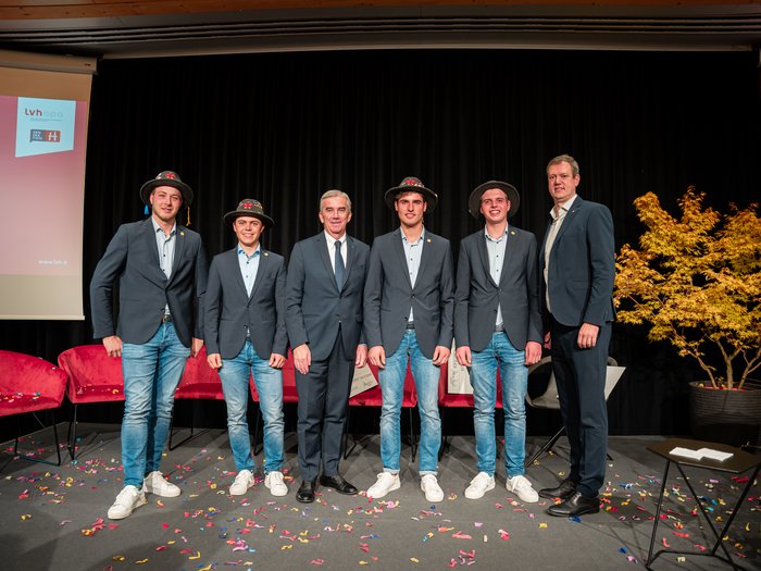 Giornata dell'artigianato Sei uomini in abito, quattro con cappelli tradizionali, su palco con coriandoli