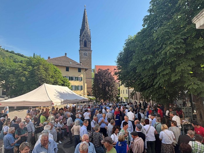63° incontro del gruppo Generazione Artigianato+: una giornata ricca di ricordi, incontri e autentico spirito di comunità Folla di persone a evento davanti a chiesa e alberi in un villaggio soleggiato