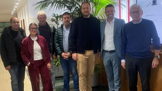 News Sieben Personen stehen in einem Flur vor einer Pflanze und einem Informationsschild