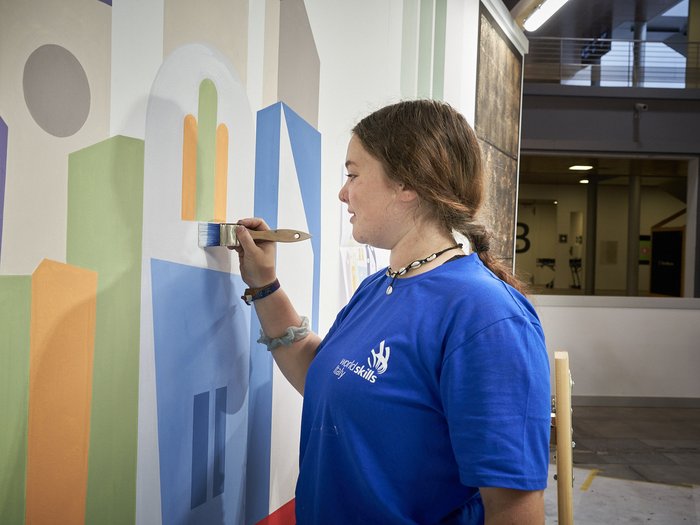 Handwerk live: Junge Talente zeigen, was sie draufhaben Junge Frau malt bunte geometrische Formen an eine Wand