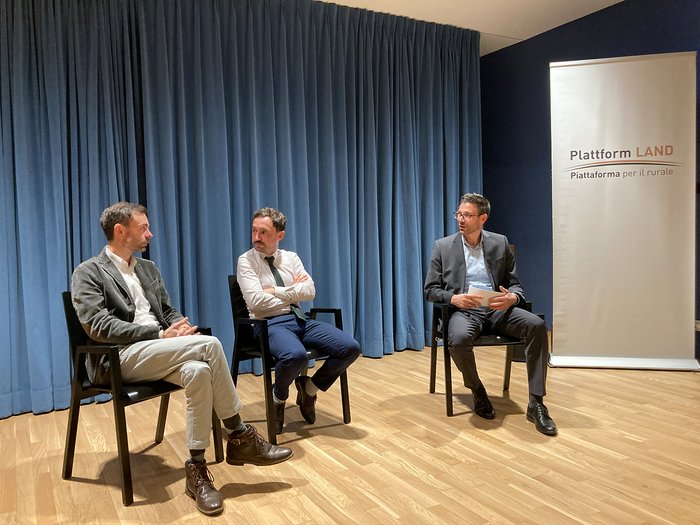 Neue Mobilität, neue Chancen für den ländlichen Raum Drei Männer sitzen auf Stühlen vor einem blauen Vorhang und einem Plakat