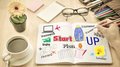 Schon angemeldet zur Kreativwerkstatt? Notizbuch mit Startup-Plan, Stiften, Brille, Kaffee und Blume auf Holztisch