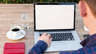 News Person arbeitet an Laptop mit leerem Bildschirm, Kaffee und Wasser auf Holztisch